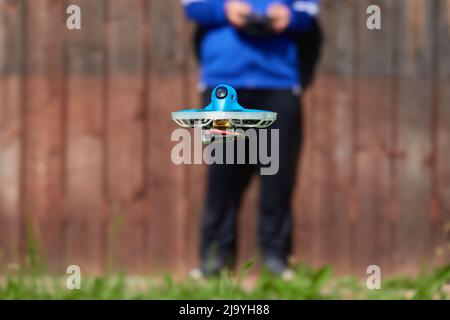 Small drone also race quad in blue is precisely controlled by the human pilot, wall in brown as background. Germany. Stock Photo