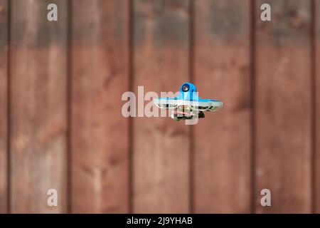 Small drone also race quad in blue, fly on brown wooden background panel Germany. Stock Photo