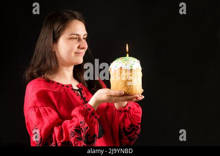 A Ukrainian woman in embroidered red national clothes holds an Easter cake on a black background Stock Photo