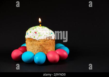 Easter cake and painted eggs on a black background with room for text, lit candle in paska Stock Photo