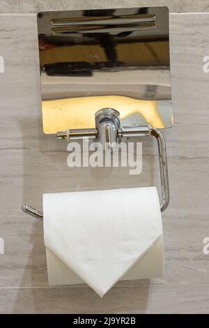 The roll of toilet paper on a holder installed on the toilet wall. Stock Photo