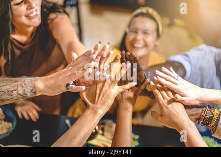 Adult friends in group, sitting around the dinner table high-fives all together celebrating friendship and to be united together - concept of lifestyl Stock Photo