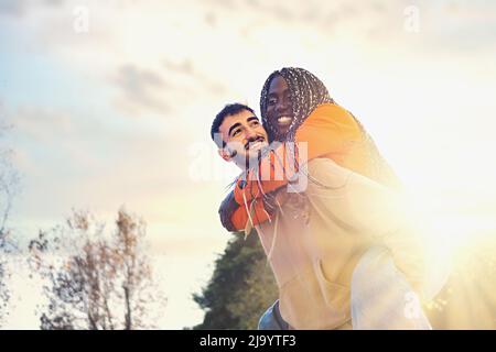 Multiethnic couple of young adults riding outdoors against the sky - people of different ethnicities engaging together - lifestyle concept Stock Photo
