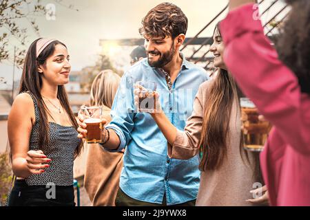 Happy multi-ethnic group of friends at university schoolmates party having fun in the terrace drinking beers and booze dancing and bonding - vivid fil Stock Photo