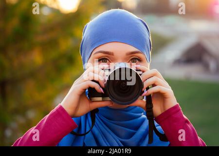 Female photographer wearing a hijab. woman holding a camera hobbyist or a journalist in summer park autumn trees forest Stock Photo