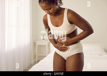 Unknown woman in white underwear experiences severe pain and abdominal  cramps at home in morning. Sick woman suffering from diarrhea, menstrual  cramps, food poisoning, gastritis or constipation. Stock Photo