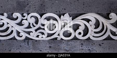White intricate cement scrolled architectural design element in between gray stone wall section Stock Photo