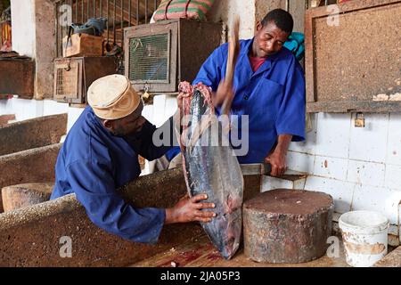 Two people working on a big fish inside the Darajani Market in Stone Town, Zanzibar, Tanzania, Africa. Stock Photo