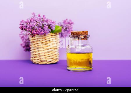 Cosmetic oil in a jar and lilac flowers on purple background. Aromatherapy, skin care concept. Selective focus. Stock Photo