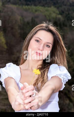 blonde woman dressed in white offering a flower to camera Stock Photo