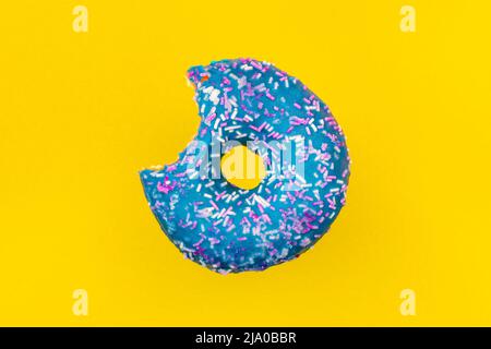 Bitten blue glazed donut with colorful sprinkles on a yellow background Stock Photo