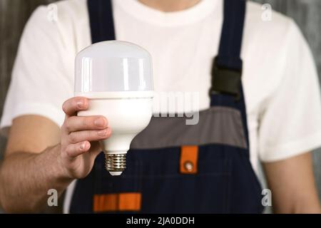 An electrician in overalls holding an energy-saving light bulb in his hands. Stock Photo