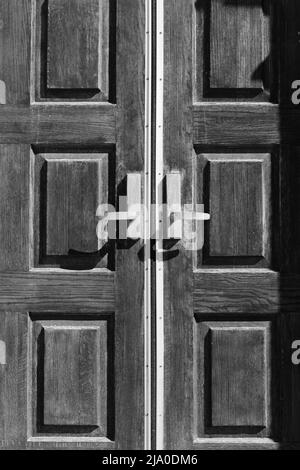 Huge and heavy wooden door with a gold handle in black and white. Stock Photo