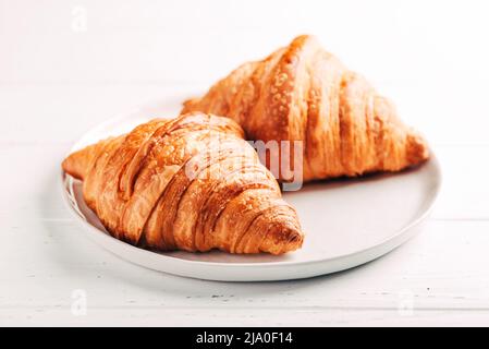 Plate with two fresh croissants on white table. Stock Photo