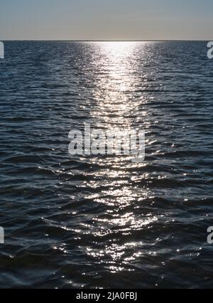 Glittering of evening sunlight reflects on sea surface. Sparkling sunlight over sea surface on waves. Sparkling water background. Stock Photo