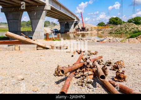 View on a heap of corrosion pipes disassembled steel scaffold joints placed on the ground at the construction site, bridge is in the background. Stock Photo