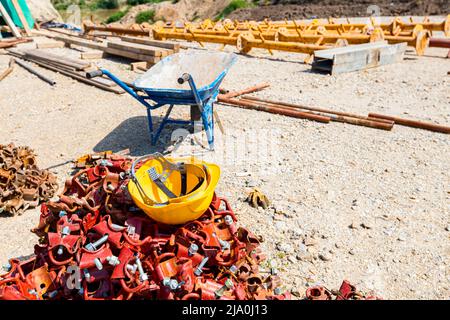 Yellow safety helmet placed on the heap of disassembled steel scaffolding joint on construction site. Stock Photo