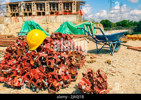Yellow safety helmet placed on the heap of disassembled steel scaffolding joint on construction site. Stock Photo