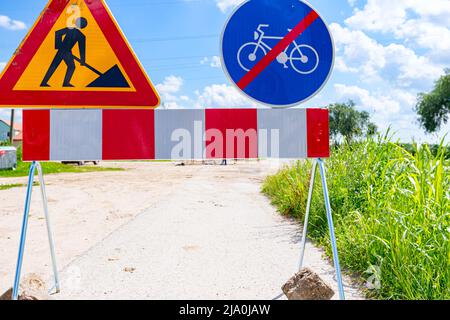 Two signs are set on the road at construction site, triangle sign, work in progress, with red and white stripes and prohibited cycling. Stock Photo