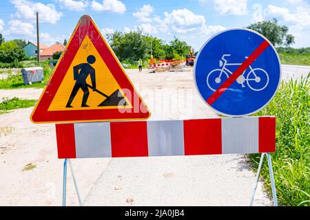 Two signs are set on the road at construction site, triangle sign, work in progress, with red and white stripes and prohibited cycling. Stock Photo