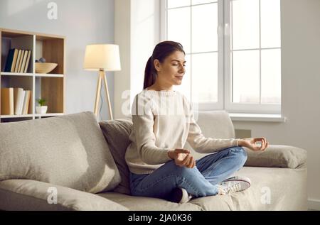 Calm woman sit on couch practice yoga Stock Photo