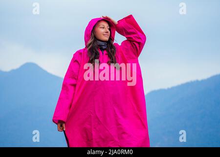 beautiful and young girl in a pink raincoat against the backdrop of the mountains. the concept of active recreation and tourism in the mountains Stock Photo