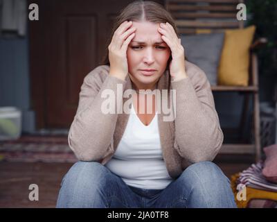 middle aged depressed woman sitting on porch. She feeling sad and worried suffering depression in mental health. Problems and broken heart concept. Stock Photo