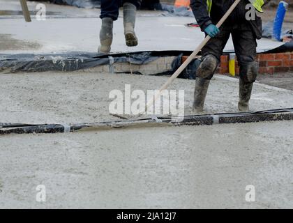 Construction workers pouring wet self leveling concrete screed during ground floor construction of a new residential house and spreading it with spazz Stock Photo