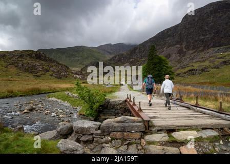 Couple hiking on the Watkin path, Snowdonia national park. Crossing bridge by Plascwmllan and beside the Afon Cwm Llan. Stock Photo