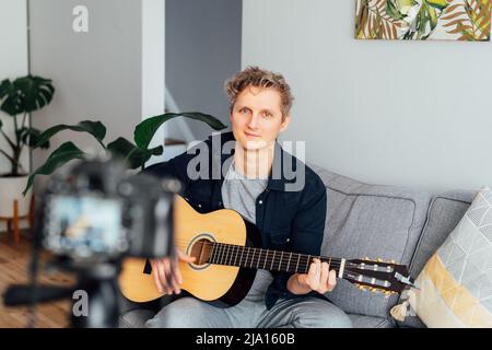Young man playing acoustic guitar and recording music video for his social networks. Amatuer musician create content at home by modern camera. Musicia Stock Photo
