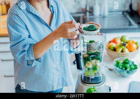 Woman adding spirulina green powder during making green smoothie on the kitchen. Superfood supplement. Healthy detox vegan diet. Healthy dieting eatin Stock Photo