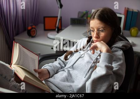 A teenage girl with braids busy reading an interesting adventure book. Stock Photo