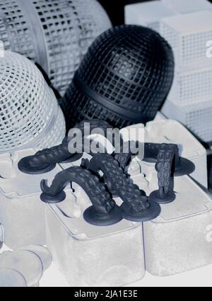Many different models printed on 3D printer. Gray and black objects printed on 3D printer made of plastic close-up. Lots of 3D printed models. Prototypes of various shapes made by 3d printer on table. Stock Photo