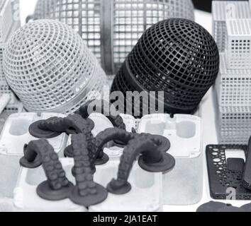 Many different models printed on 3D printer. Gray and black objects printed on 3D printer made of plastic close-up. Lots of 3D printed models. Prototypes of various shapes made by 3d printer on table. Stock Photo