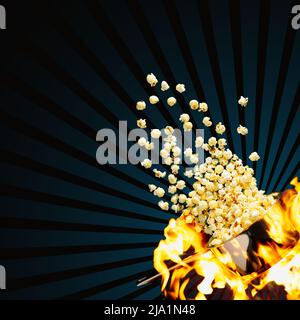 Flying popcorn on a dark background. Hot popcorn flying from pot under fire. Advertising concept. Stock Photo