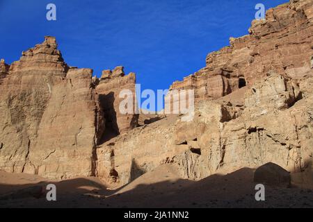 A huge high wall with embossed towers in the Charyn canyon against the background of a sky with light clouds in summer, sunny Stock Photo