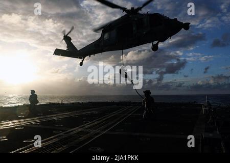 May 11, 2022 - Philippine Sea - Sailors, assigned to Explosive Ordnance Disposal Mobile Unit (EODMU) 3, rope down from an MH-60S Sea Hawk helicopter, assigned to the Chargers of Helicopter Sea Combat Squadron (HSC) 14, onto the Ticonderoga-class guided-missile cruiser USS Mobile Bay (CG 53) during a helicopter visit, board, search and seizure (HVBSS) training. Abraham Lincoln Strike Group is on a scheduled deployment in the U.S. 7th Fleet area of operations to enhance interoperability through alliances and partnerships while serving as a ready-response force in support of a free and open Indo- Stock Photo