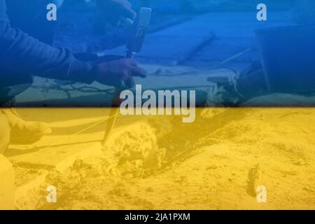 Defocus bricklayer removing irregularities on floor screed with hammer and chisel. Male hands in red work gloves hold a hammer and chisel. Rebuild Ukr Stock Photo