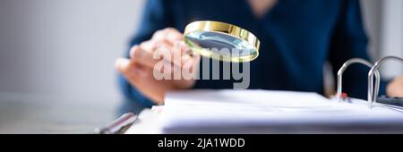 Close-up Of A Businesswoman's Hand Checking Bill Through Magnifying Glass At Workplace Stock Photo