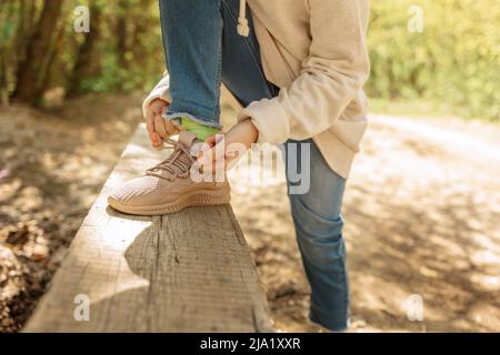 Cute sporty runner girl in fashion activewear wearing floral cap and pink leggings  outfit getting ready for jogging tying laces running shoes on grass park.  Fitness woman living active lifestyle. Stock Photo