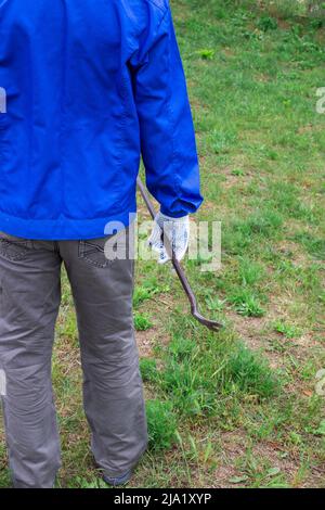 Worker in blue overalls with iron pry bar outdoors. Repair and services of the master. Stock Photo