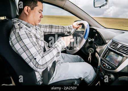 Man sitting in his car texting with his cell phone, Side view of a young man sitting inside car using mobile phone, Young man sitting in a car and Stock Photo