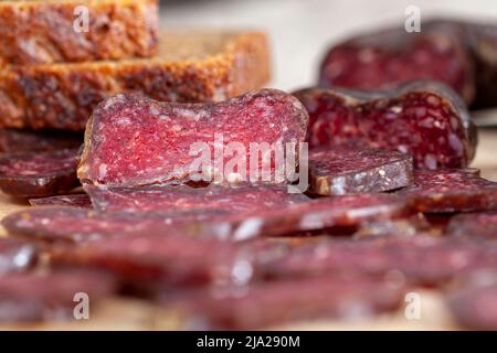 sliced piece of cured sausage on the table, dried pork meat cut into chunks on the table Stock Photo