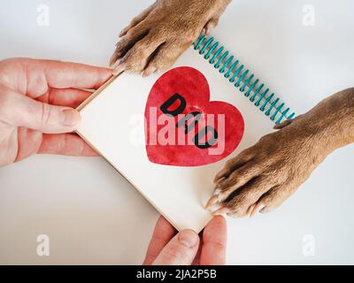 Dog paws, male hands, beautiful pattern in the form of a heart and word DAD. Close-up, indoors. Congratulations for family, loved ones, friends and co Stock Photo