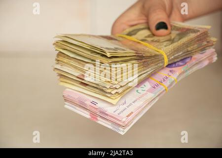 A woman's hand holds a stack of Ukrainian hryvnias, giving money, one hundred and two hundred hryvnias in her hand Stock Photo
