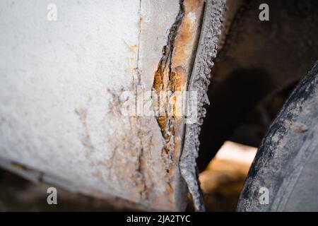 Rusted fender of a white car close-up. The effect of reagents in winter on an unprotected car body. rotten metal Stock Photo