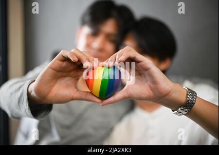 Close-up image, Two asian gay men couple holding a rainbow heart and making a heart shape with hands. LGBT love symbol. Stock Photo