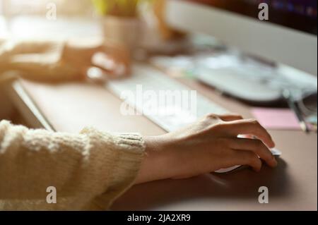 Female office worker or business employee sits at her office desk, working, managing her task on computer and using wireless mouse. cropped image Stock Photo