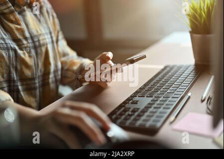 Close-up shot, Female office worker working at her office desk, holding smartphone and using computer. Stock Photo