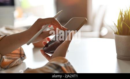 Female hands holding a smartphone and stylus pen, using smartphone, searching some information on the internet. cropped image Stock Photo